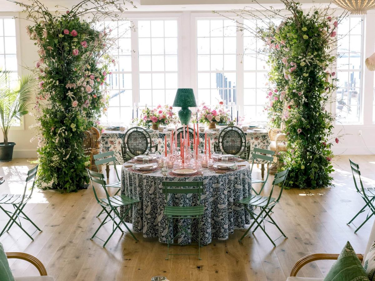 An elegantly decorated RI event venue with round tables, floral arrangements, greenery, and large, bright windows.