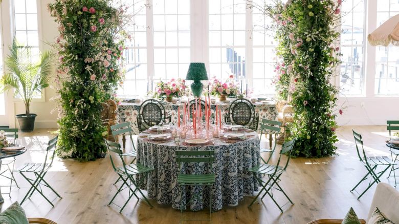 An elegantly decorated RI event venue with round tables, floral arrangements, greenery, and large, bright windows.